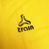 Una tela de color amarillo vibrante con un diseño texturizado muestra un logotipo estilizado en forma de llama negra sobre el texto en minúscula "Peto Malla Train".