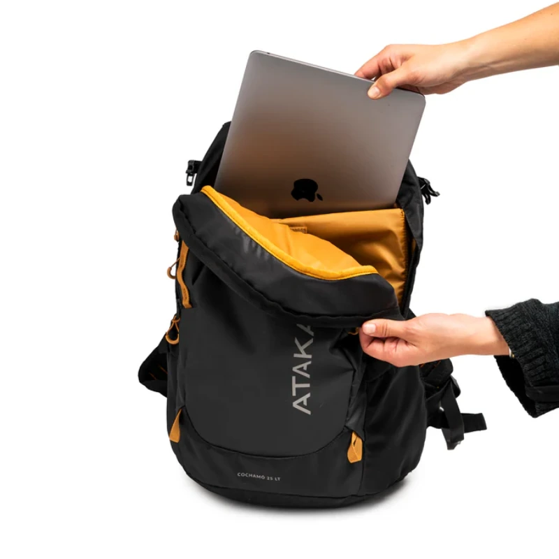 Una mano desliza una computadora portátil dentro de la mochila negra Mochila Atakama Outdoor Cochamó 25L, que presenta un interior amarillo vibrante y "ATAK" en el bolsillo frontal, lo que la hace perfecta para aventuras al aire libre.