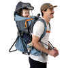 Un hombre con gorra y camisa blanca lleva a un niño pequeño en una mochila portabebé Atakama Outdoor Leonera de color azul. El niño está sentado cómodamente con una sombrilla y la mochila tiene bolsillos y una botella de agua adjunta, lo que hace que ambos parezcan estar listos para una aventura al aire libre.