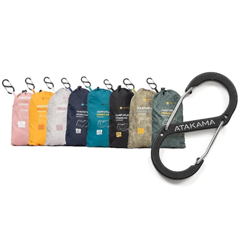 Una colección de hamacas vibrantes y compactas que se presenta en bolsas individuales con mosquetones adjuntos, en una variedad de colores y diseños. A la derecha, un mosquetón negro grande muestra de manera prominente la marca "Atakama Outdoor".