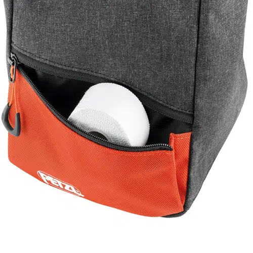 Una mochila en gris y naranja vibrante, similar a la Bolsa Petzl para Magnesio Sakab, tiene un bolsillo inferior con cremallera ligeramente abierto para revelar un rollo de papel higiénico blanco, con el logotipo de la marca destacado en la sección naranja brillante.