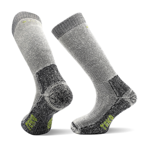Un par de calcetines grises gruesos hasta la rodilla, los Calcetín Teko EcoExpedition Extra Heavy Full Cushion 5.0, que cuentan con áreas de talón y puntera reforzadas. Presentan secciones de color gris oscuro en el tobillo, el talón y la puntera con pequeños detalles verdes cerca de la suela y el borde superior.