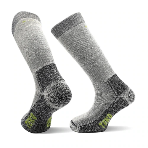 Un par de calcetines grises gruesos hasta la rodilla, los Calcetín Teko EcoExpedition Extra Heavy Full Cushion 5.0, que cuentan con áreas de talón y puntera reforzadas. Presentan secciones de color gris oscuro en el tobillo, el talón y la puntera con pequeños detalles verdes cerca de la suela y el borde superior.