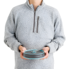 Se muestra a una persona con un suéter gris sosteniendo una Olla Plegable Sea To Summit Frontier de 1,3 l, un recipiente hermético redondo de color gris y verde azulado con tapa y asa con cierre, sobre un fondo blanco liso. Este recipiente es ideal para almacenar alimentos.