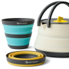 Explora el juego de cocina de 3 piezas Sea To Summit Frontier con una taza plegable turquesa y gris, una tetera beige y amarilla con asa negra y dos tazones apilables de color gris mostaza. Ideal para aventuras en movimiento.