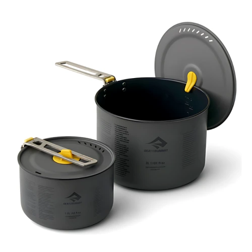 Se muestra un juego de dos ollas para cocinar Sea To Summit Frontier de color gris oscuro con asas amarillas plegables y tapas extraíbles, una más pequeña y otra más grande. Ambas ollas tienen marcas de medición en los costados y un logotipo que dice "SEA TO SUMMIT". La tapa de la olla más grande está ligeramente entreabierta. Este juego de ollas Sea To Summit Frontier de 2 piezas es perfecto para aventuras al aire libre.