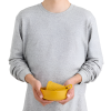 Sobre un fondo blanco liso, una persona que viste una sudadera gris sostiene un recipiente de plástico amarillo que cuenta con un colador y un asa incorporados, del juego de cocina de 6 piezas Sea To Summit Passage.