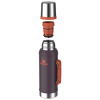 Botella térmica Stanley Classic de 950 ml en color ciruela con asa y el logotipo de la marca en color naranja. La tapa y el tapón se ciernen sobre ella, mientras que los detalles plateados y naranjas realzan la elegancia metálica de su interior.