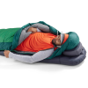 Una persona disfruta de una siesta al aire libre en un saco de dormir verde y gris Sea To Summit Ascent -9 °C sobre un colchón inflable, vistiendo un gorro gris, una camiseta naranja y mangas largas grises. El entorno parece tranquilo y pacífico.