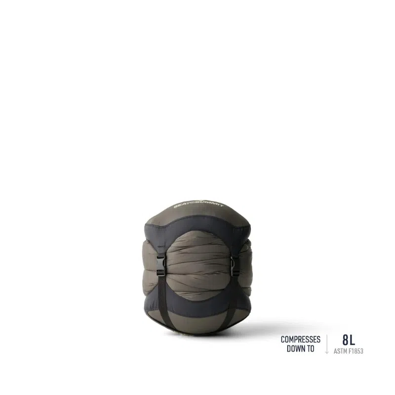 El saco de dormir Pluma Sea To Summit Spark Women's -9°C es un saco de dormir compacto en un tono oscuro, comprimido de manera experta en una forma redonda con correas. El texto en el producto indica que se puede compactar hasta 8 litros y el fondo blanco liso acentúa su diseño elegante y eficiente.
