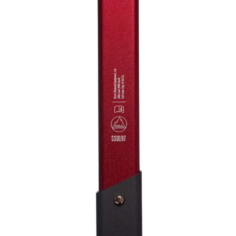 Vista en primer plano del mango del piolet Pala Transfer Black Diamond en Hyper Red y negro, con especificaciones grabadas junto con un logotipo y un número de serie. El mango incluye un perno cerca de la parte inferior.