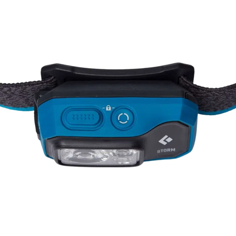 La Linterna Frontal Black Diamond Storm 450lm es una linterna frontal LED azul compacta con una correa negra ajustable, que presenta un botón circular y un icono de candado en la parte delantera. El lado derecho muestra elegantemente la palabra "Storm" junto a un pequeño logotipo.