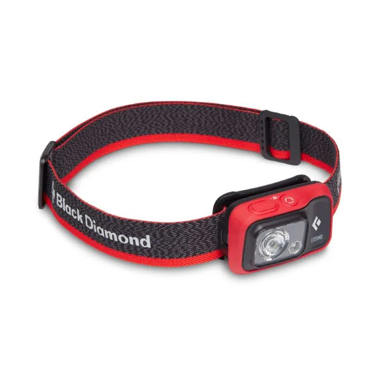 La Linterna Frontal Black Diamond Cosmo 350lm presenta un elegante diseño en rojo y negro con una correa ajustable, cuenta con una potente luz LED redonda y lleva la icónica etiqueta "Black Diamond" en el costado, lo que la hace perfecta para cualquier aventura.