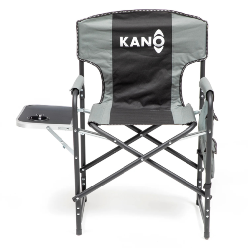 La "Silla Plegable Kano con Mesa y Bolsillos Puclaro" es una silla de director plegable negra y gris con una mesa auxiliar, ideal para cualquier entorno al aire libre. Tiene el nombre "KANO" en el respaldo, incluye un portavasos en su mesa auxiliar y tiene un marco de metal negro resistente.