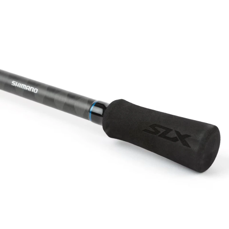 El primer plano muestra el elegante diseño de la caña Shimano SLX Spinning de 2,10 m, que cuenta con una empuñadura negra con las palabras "Shimano" y "SLX" claramente visibles. Un anillo con detalles en azul cerca del mango le suma un aspecto elegante.