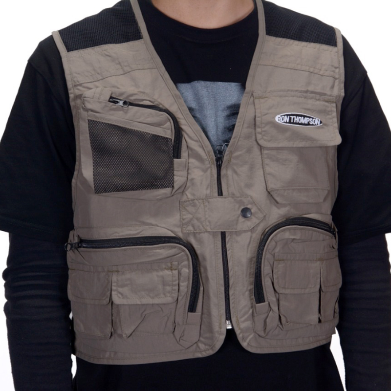 Con el chaleco de pesca Ron Thompson Mesh Lite, esta persona luce un chaleco táctico gris con múltiples bolsillos con cierre y un parche prominente, combinado con una camisa negra de manga larga debajo.