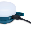 Un modelo compacto y redondo de linterna recargable Moji R+ de Black Diamond de color azul con una tapa blanca se carga mediante un cable USB negro. Este dispositivo tiene una tapa cerrada parcialmente visible y luces indicadoras.