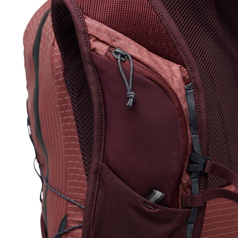 Primer plano de una mochila "Mochila" color granate, con compartimentos con cierre y correas ajustables. La tela presenta un diseño texturizado con estampado Black Diamond.