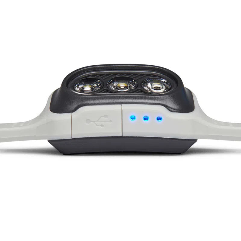 Primer plano de la elegante Linterna Frontal Black Diamond Deploy 325lm, que cuenta con tres luces circulares en la parte superior y emite una luminosidad de 325 lúmenes. El diseño se moderniza aún más con tres luces indicadoras azules y un símbolo USB en el lateral que sugiere opciones de conectividad versátiles.