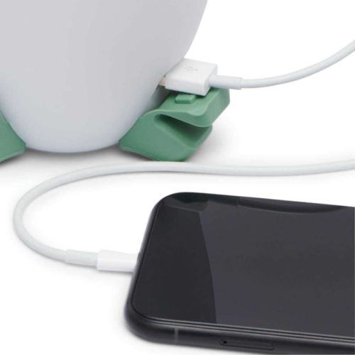 Un teléfono inteligente conectado a un cable de carga, que está enchufado a un dispositivo blanco similar al Black Diamond Orbiter 450lm. El cable, asegurado por un organizador verde, contrasta con el teléfono que está fuera de la pantalla, haciendo eco del diseño elegante de este producto.