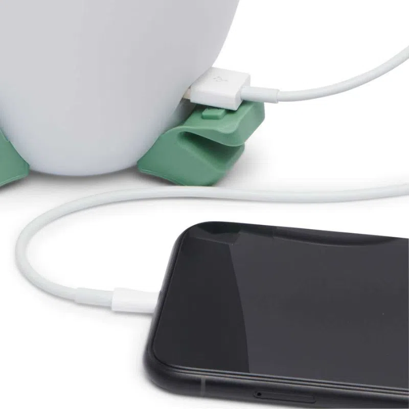 Un teléfono inteligente conectado a un cable de carga, que está enchufado a un dispositivo blanco similar al Black Diamond Orbiter 450lm. El cable, asegurado por un organizador verde, contrasta con el teléfono que está fuera de la pantalla, haciendo eco del diseño elegante de este producto.