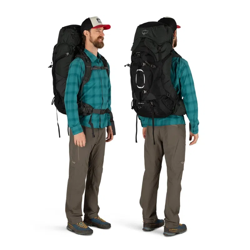 Un hombre muestra la Mochila Osprey Aether 65L mientras viste una camisa a cuadros verde, pantalones grises, zapatos de senderismo y una gorra negra con una parte superior roja. Está fotografiado tanto de frente como de perfil sobre un fondo blanco liso.