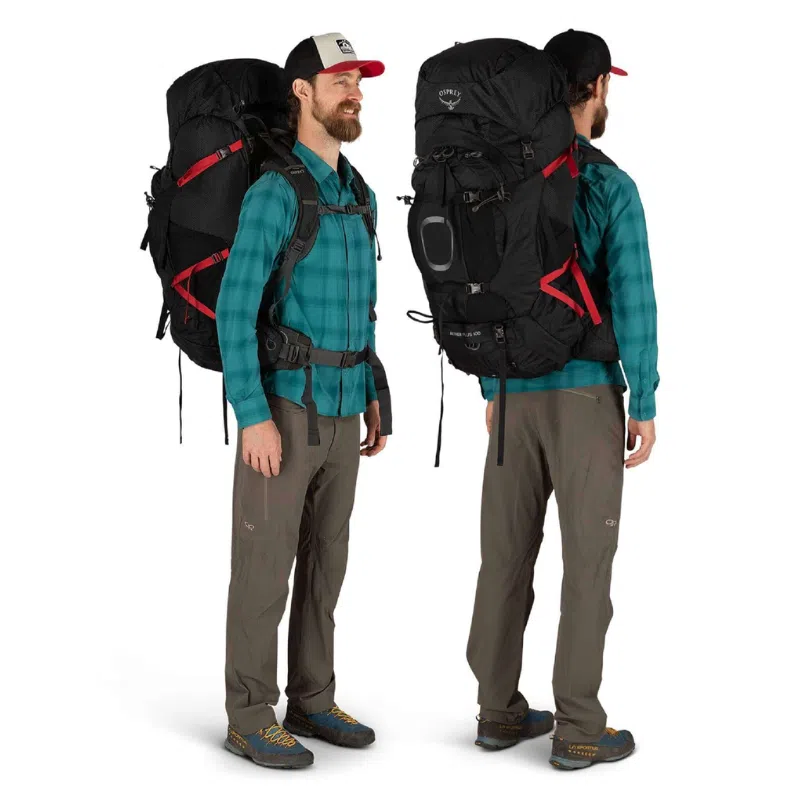 Un hombre que viste una camisa de cuadros azules, pantalones marrones y una gorra negra lleva una mochila de senderismo grande Mochila Osprey Aether Plus 85L con correas rojas. La imagen lo captura tanto de frente como de atrás, resaltando los detalles meticulosos de la mochila.
