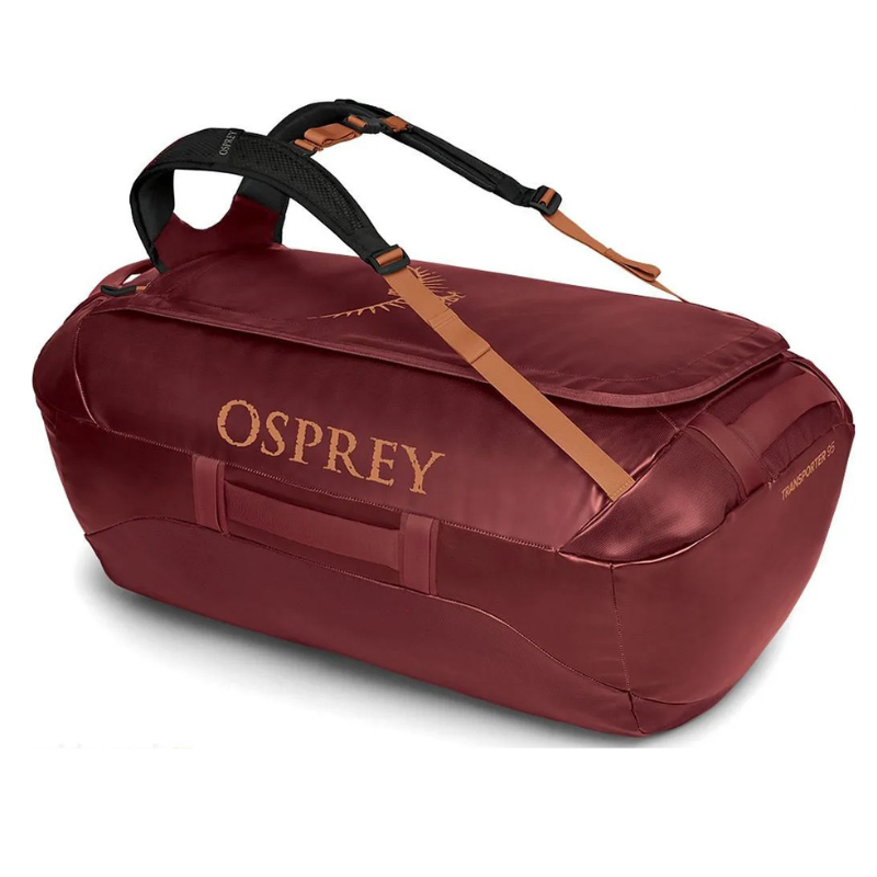 El bolso de transporte Osprey Duffel 95, en color granate, está equipado con correas de hombro ajustables en negro y marrón y cuenta con un compartimento principal con cierre de cremallera y asas laterales. El logotipo de Osprey se muestra de forma destacada en el lateral de este bolso. Se presenta elegantemente sobre un fondo blanco liso.