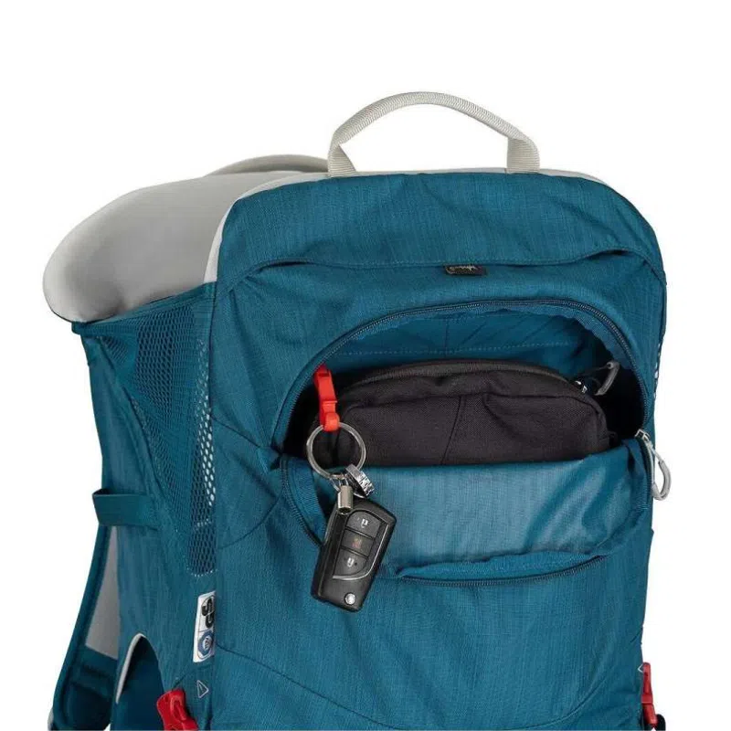 La mochila portabebé Osprey Poco SLT de color azul tiene un bolsillo frontal ligeramente abierto que deja al descubierto un bolso negro en el interior. En el tirador de la cremallera del bolsillo se encuentra una llave de coche con un clip rojo. Esta versátil mochila portabebé también viene equipada con un asa superior y bolsillos laterales de malla para mayor comodidad.