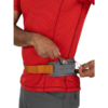 Una persona que viste una camisa roja y un pantalón gris se ajusta el cinturón para correr Osprey Duro Dyna LT Belt, que incluye una bolsa gris en la cintura con una correa naranja. Está insertando o quitando un clip de mosquetón de este práctico accesorio.