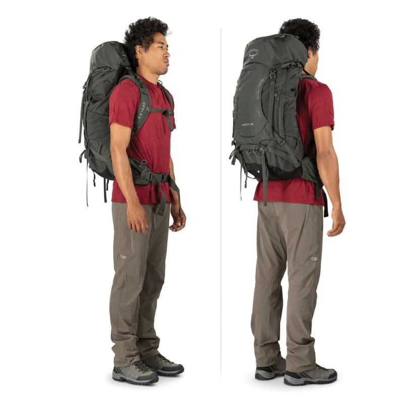 Una persona vestida con una camisa roja, pantalones marrones y botas de montaña se mantiene de pie con confianza sosteniendo una gran mochila negra. Las vistas laterales enfatizan las correas y el diseño de la Mochila de Senderismo Osprey Kestrel 38 (copia), destacando su durabilidad y estilo para cualquier aventura.