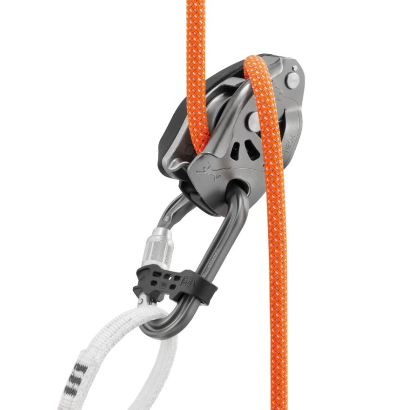 Un dispositivo de aseguramiento para escalada incluye un mosquetón de seguridad Petzl Attache Bar conectado a una cuerda de color naranja y blanco. El dispositivo plateado presenta detalles en negro, diseñado para controlar la tensión de la cuerda durante las actividades de escalada, lo que garantiza una seguridad de primer nivel.