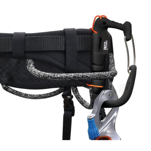 Primer plano de un arnés Petzl negro con el Portatornillos Universal Petzl Caritool Evo, un dispositivo de aseguramiento acoplado y un mosquetón. El arnés presenta detalles de cuerda tejida y correas de seguridad para una máxima seguridad.