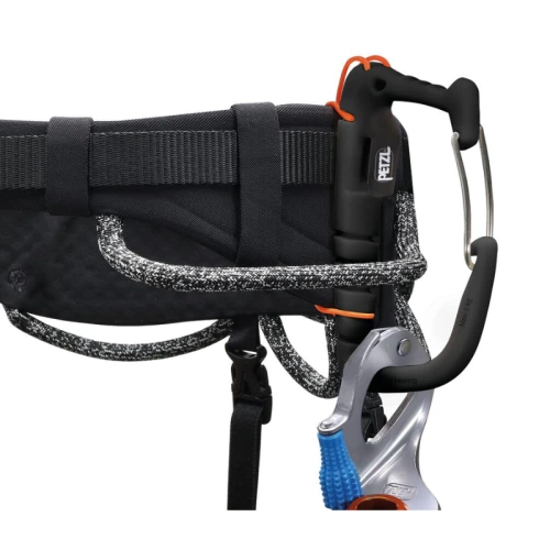 Primer plano de un arnés Petzl negro con el Portatornillos Universal Petzl Caritool Evo, un dispositivo de aseguramiento acoplado y un mosquetón. El arnés presenta detalles de cuerda tejida y correas de seguridad para una máxima seguridad.