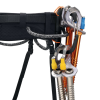 Primer plano de un equipo de escalada en hielo en un arnés negro con detalles en gris, que muestra cintas exprés, dos tornillos para hielo con detalles en naranja y correas de cincha. El arnés cuenta con el sistema Petzl Caritool Evo para una organización eficiente. El equipo está asegurado de forma experta para su uso.