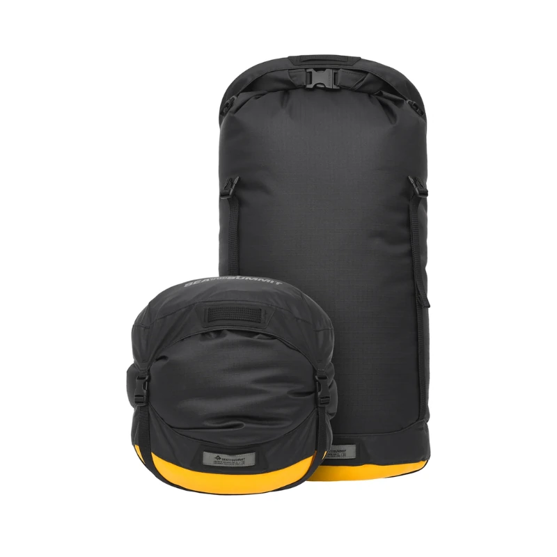 Se muestran dos bolsas impermeables negras con bases amarillas. La más grande, cilíndrica, tiene un cierre superior enrollado como la Bolsa de Compresión Evac Compression Dry Bag HD, mientras que la más pequeña es redonda. Ambas tienen etiquetas de marca visibles y están diseñadas para uso en exteriores para mantener el equipo seguro y seco.