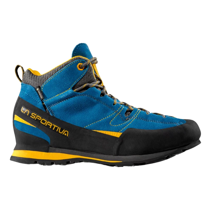 Sobre un fondo blanco, la zapatilla de aproximación La Sportiva Boulder X Mid GTX en azul y negro con detalles y cordones amarillos muestra su resistente suela para exteriores y la marca "La Sportiva" en el lateral.