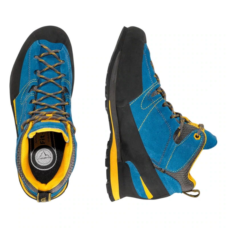 Las botas La Sportiva Boulder X Mid GTX en azul y negro presentan detalles en amarillo. Una de las botas se muestra de arriba hacia abajo, mostrando los cordones y el forro interior, mientras que la otra está de lado para resaltar la suela resistente y los detalles de las costuras.