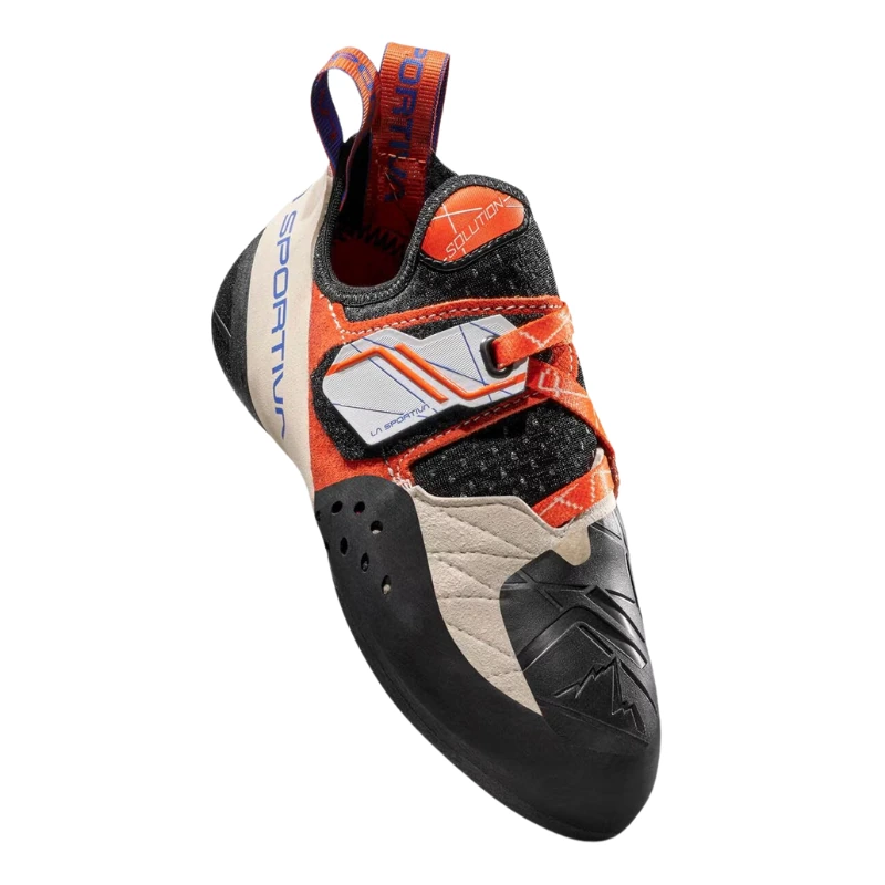 La zapatilla de escalada La Sportiva Solution (copia) es un calzado de escalada gris y negro con detalles en naranja, que cuenta con una correa de velcro y una suela de goma texturizada. Incluye patrones geométricos blancos y la marca en el costado y la lengüeta para un estilo adicional.