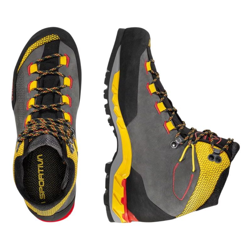 Las botas de montaña La Sportiva Trango Tech Leather GTX, con detalles en gris, negro, amarillo y rojo, se muestran con el zapato izquierdo mostrando cordones desde la parte superior y el nombre de la marca en la plantilla, mientras que el zapato derecho en ángulo resalta su banda de rodadura y diseño lateral.