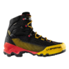 La Sportiva Aequilibrium ST GTX es una bota de senderismo resistente con parte superior de malla negra, detalles en amarillo y rojo y suela gruesa. Tiene cordones amarillos y la marca "La Sportiva" en el lateral.