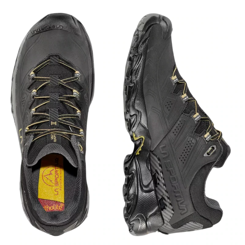Un par de zapatillas de montaña La Sportiva Ultra Raptor II Leather GTX negras con suelas resistentes y detalles en amarillo. Una de las zapatillas se ve de lado y la otra de arriba hacia abajo, mostrando el diseño con cordones y la plantilla con la marca. Ideales para cualquier aventura en la montaña.