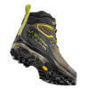 La bota de trekking La Sportiva TX Hike Mid GTX está inclinada hacia arriba y muestra su suela resistente, tela de malla verde y negra con detalles amarillos como una presilla trasera. La marca "La Sportiva" se muestra en el lateral.