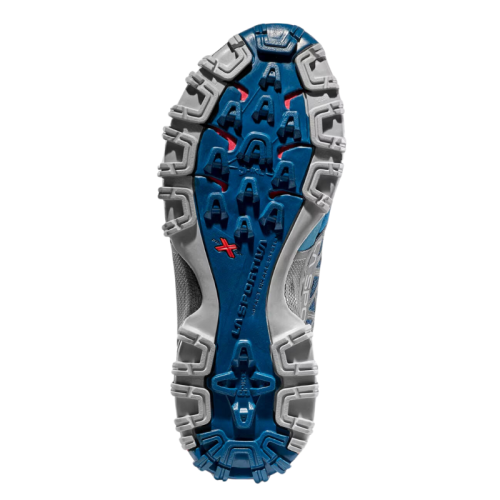 La imagen muestra la suela rugosa de una zapatilla deportiva La Sportiva azul y gris, perfecta para aventuras en la montaña. La marca "La Sportiva" está grabada en el centro, con detalles en rojo. Este modelo es Bushido II Mujer.