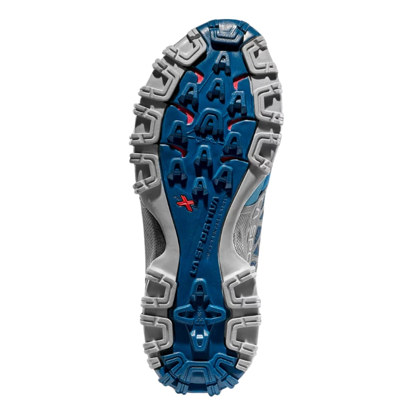 La imagen muestra la suela rugosa de una zapatilla deportiva La Sportiva azul y gris, perfecta para aventuras en la montaña. La marca "La Sportiva" está grabada en el centro, con detalles en rojo. Este modelo es Bushido II Mujer.