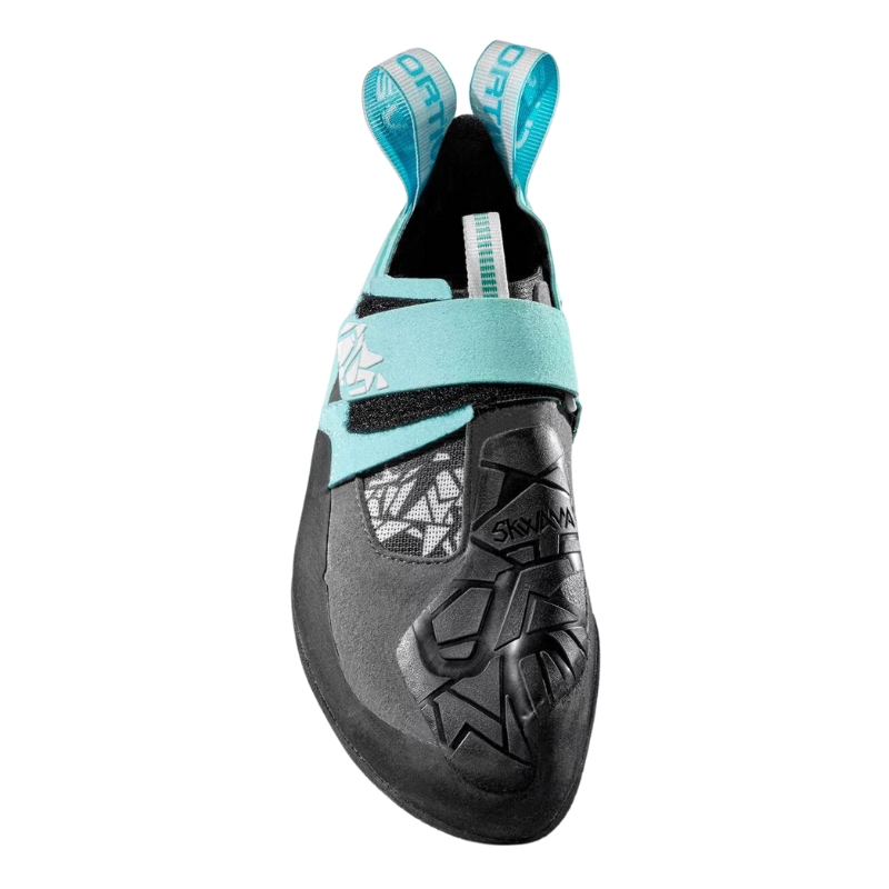 La zapatilla de escalada La Sportiva Skwama Vegan presenta un llamativo diseño en turquesa y negro con patrones geométricos, una correa de velcro segura, una suela de goma prominente y dos cómodas presillas en el talón para facilitar su uso.
