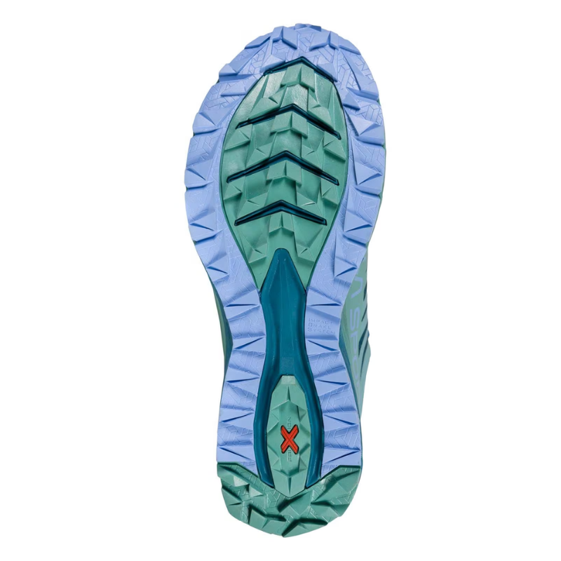 La suela de la Zapatilla de Mountain Running La Sportiva Jackal Mujer presenta una banda de rodadura de color azul claro y verde con ranuras profundas para tracción, además de una pequeña X roja en el talón que muestra su diseño detallado y enfoque en el rendimiento.