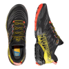 Un par de zapatillas de montaña La Sportiva Akasha II en negro y amarillo. La zapatilla izquierda se ve desde arriba y la derecha desde un costado. Los cordones naranjas y amarillos llamativos con patrones intrincados crean una apariencia dinámica y deportiva.
