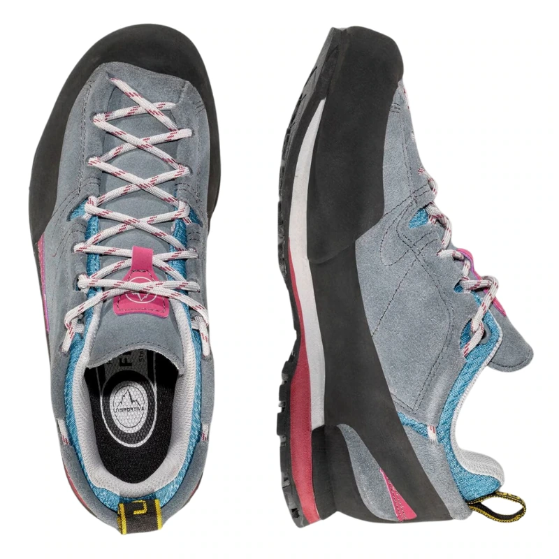 Se muestra un par de zapatos de escalada Zapatilla de Aproximación La Sportiva Boulder X Mujer en color gris con detalles en rosa y azul, uno de lado mostrando la suela y el diseño, y el otro desde arriba resaltando los cordones y los detalles de la lengüeta.