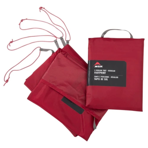La huella de la carpa roja MSR para Carpa MSR Remote 2 (copia) está cuidadosamente doblada con cables adjuntos visibles, y el embalaje muestra de manera prominente una etiqueta que dice "Huella de carpa para 2 personas".